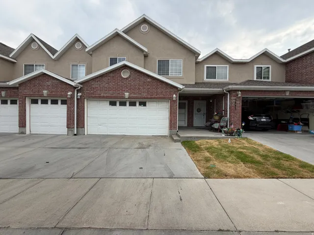 Two-story residence featuring brick and stucco exterior, multiple gables, white garage doors with window inserts, and concrete driveways