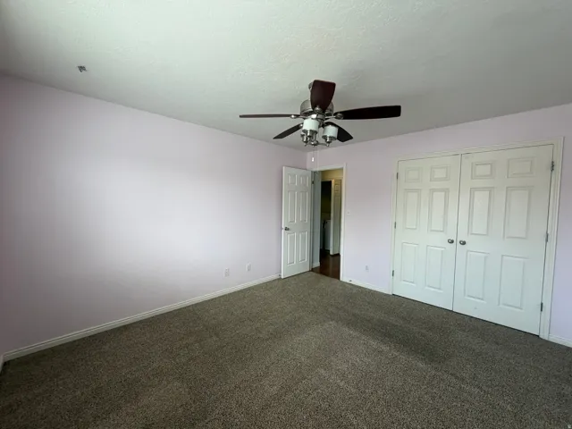 Expansive room featuring textured carpeting, a ceiling fan with integrated lighting, and double bi-fold closet doors