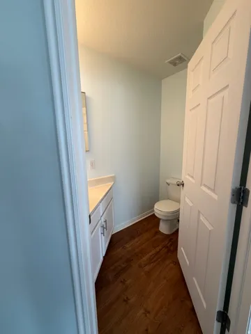 White vanity with polished chrome hardware, light-toned countertop, wood-finish flooring, and a white toilet