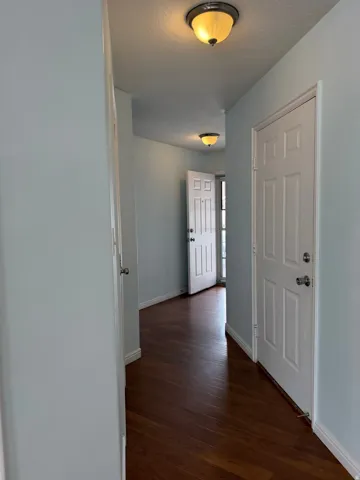 Hallway featuring wood-finish flooring, light blue wall paint, white interior doors, and flush-mount ceiling lights