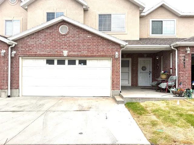 Brick facade with stucco accents, attached garage with window inserts, covered front entry, concrete driveway, and front landscaping