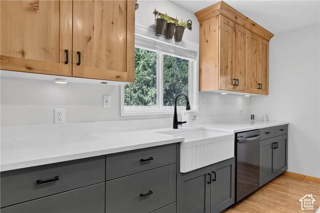 Two-tone cabinetry with light wood upper cabinets and dark gray lower cabinets, white countertops, white apron-front sink, black gooseneck faucet, and stainless steel dishwasher