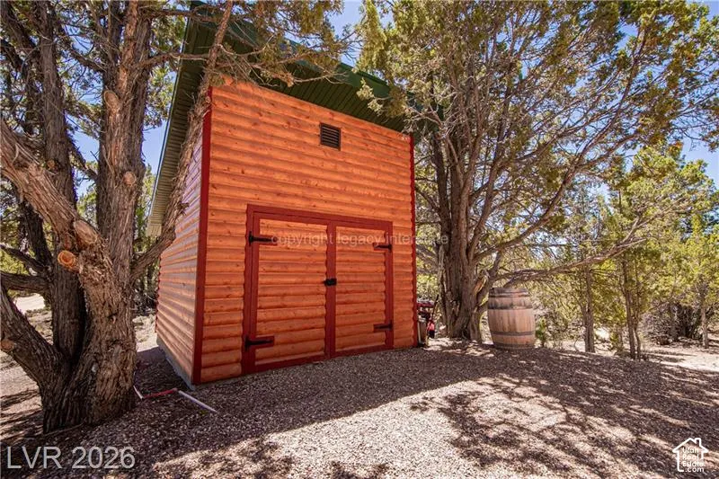 Wood-sided outbuilding with dual doors, a gravel ground surface, and surrounded by mature trees