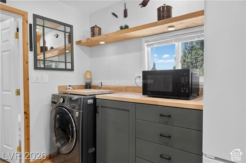 Built-in cabinetry with dark hardware, natural wood-finish countertops, floating wood-finish shelving with integrated lighting, and a white framed window