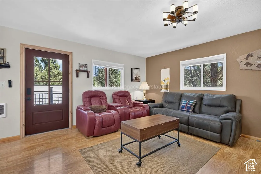 Wood-finish flooring, accent wall, modern ceiling light fixture, multiple windows, and a glass-paneled exterior door