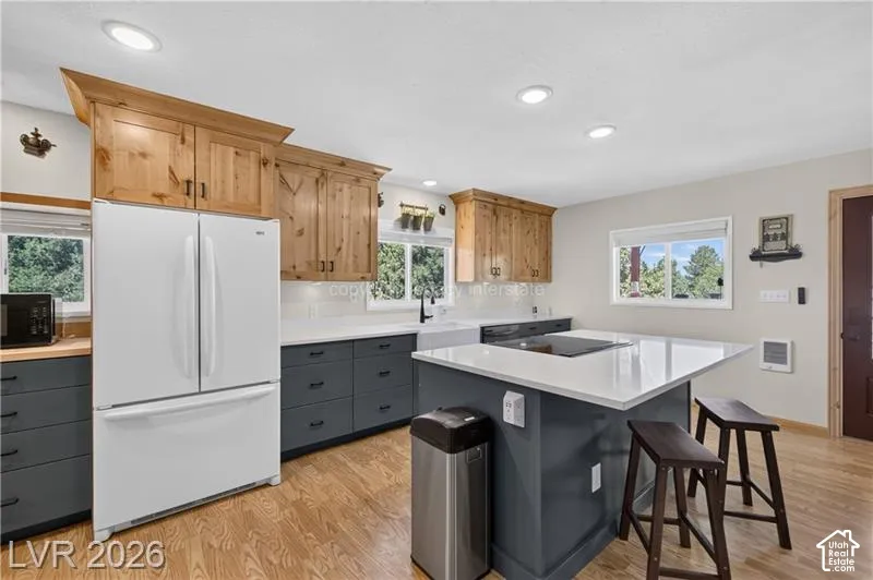 Kitchen featuring wood-finish flooring, recessed lighting, wood cabinetry, dark gray lower cabinetry, and a center island with a white countertop