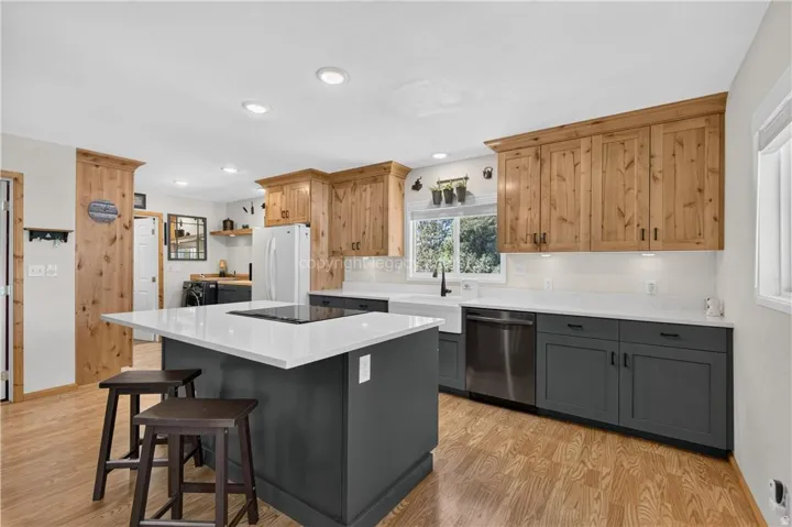 Wood-finish flooring throughout, complemented by a central island with a white countertop and integrated cooktop