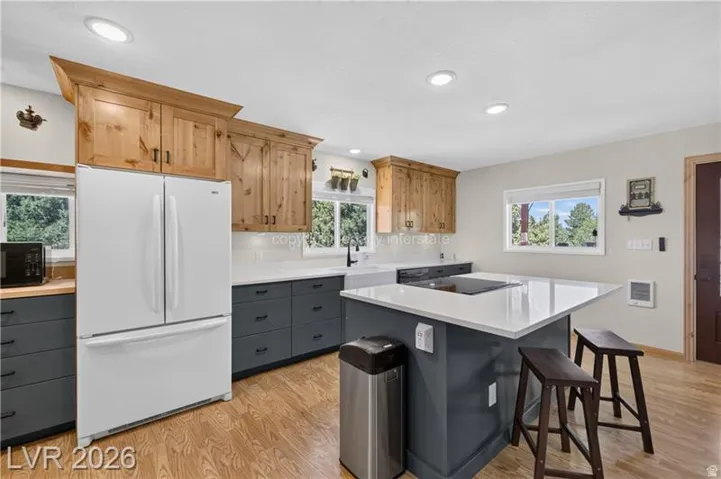 Kitchen featuring wood-finish flooring, recessed lighting, wood cabinetry, dark gray lower cabinetry, and a center island with a white countertop