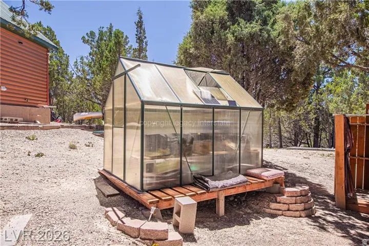 Freestanding greenhouse with an automatic roof vent, solar panel, and wood platform base