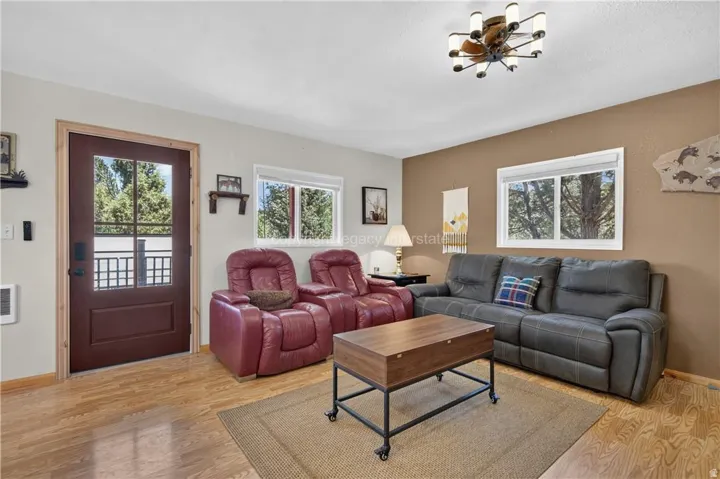 Wood-finish flooring, accent wall, modern ceiling light fixture, multiple windows, and a glass-paneled exterior door