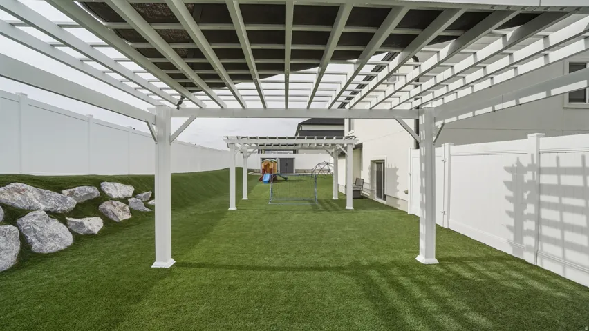 Expansive outdoor space featuring a white pergola, artificial turf, perimeter fencing, and a rock-lined terraced area