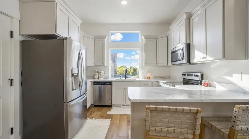 White shaker cabinetry with crown molding, stainless steel appliances, light wood-finish flooring, and white countertops