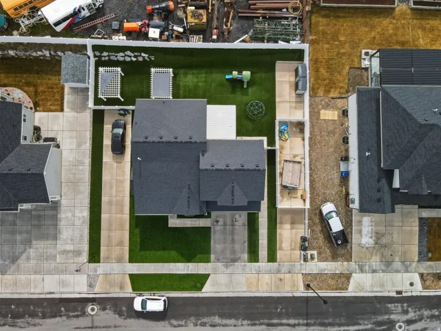 Contemporary residence with a dark shingled roof, a paved driveway, and a fenced backyard featuring artificial turf