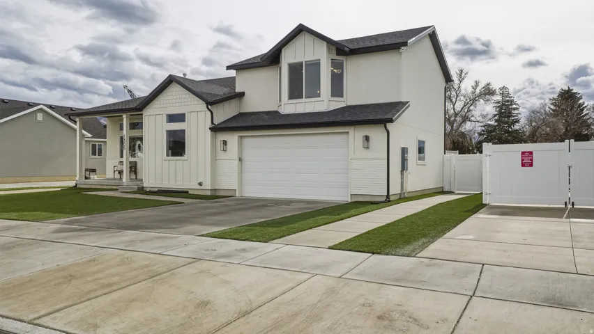 Two-story home with a two-car garage, white vertical siding, dark roof, and a concrete driveway