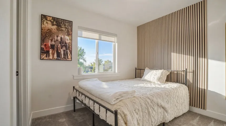 Textured accent wall, neutral wall paint, window with roller shade, gray carpet flooring, and white trim