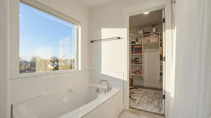 Built-in soaking tub with subway tile surround, large window, and brushed nickel fixtures