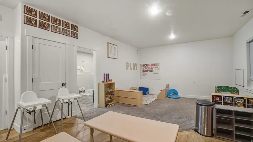 Bright, open playroom with neutral walls, recessed lighting, and wood-finish flooring throughout