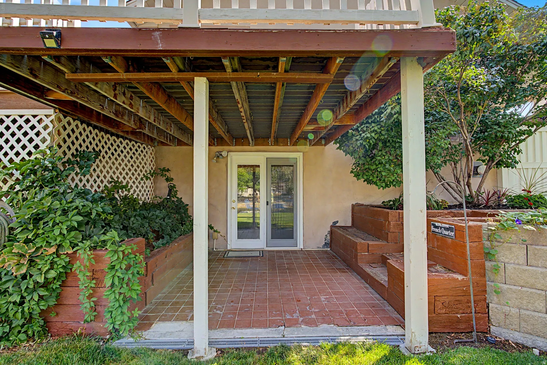 Covered patio featuring red brick-style flooring, white lattice detailing, and multi-level wood planters