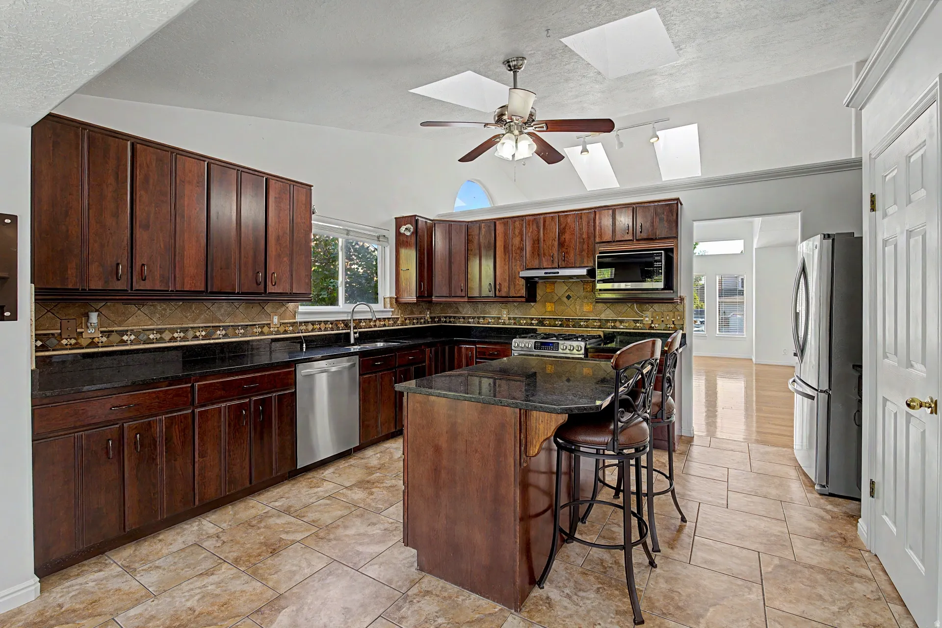 Kitchen featuring extensive dark wood-finish cabinetry, black countertops, stainless steel appliances, and a tiled backsplash