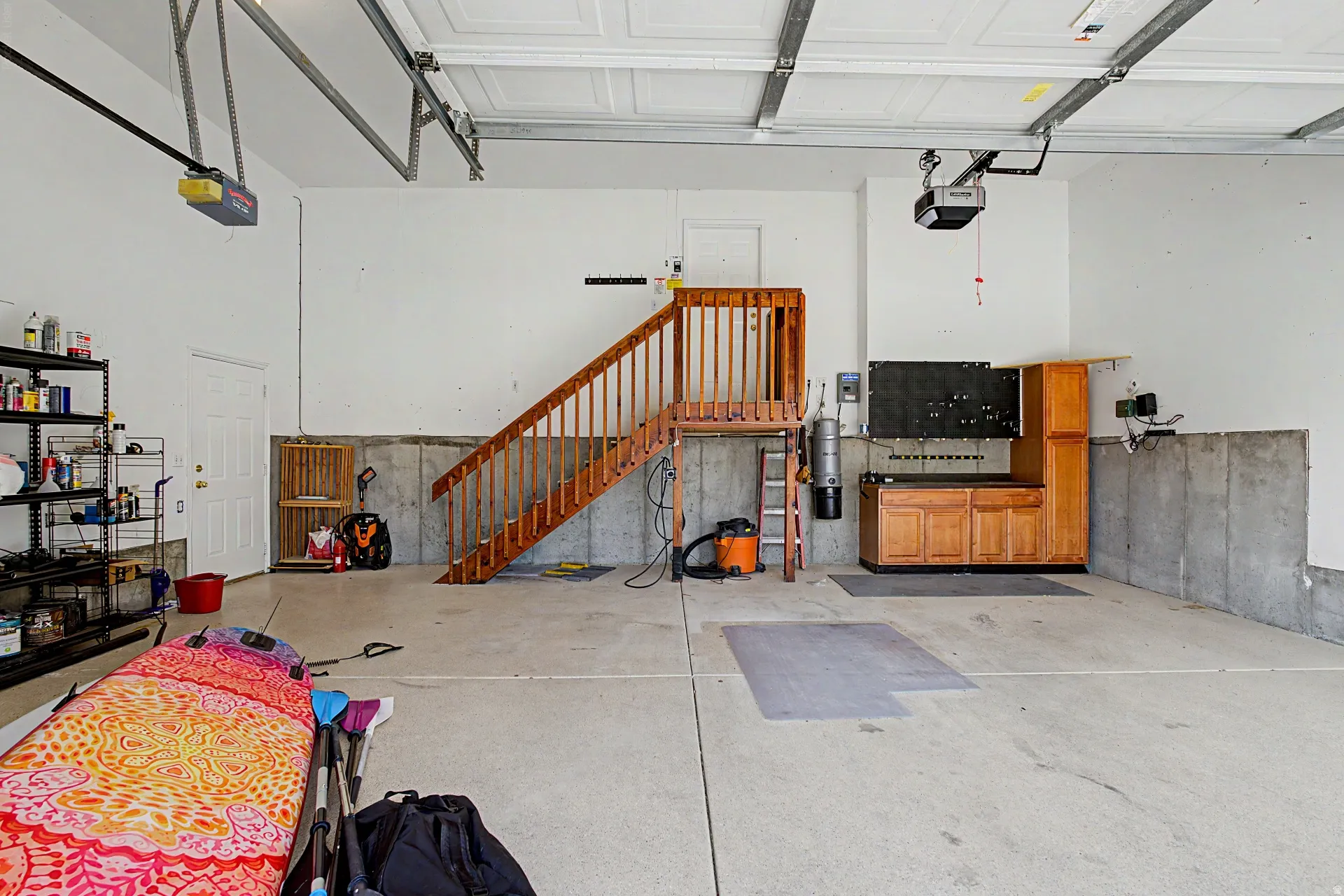 Concrete flooring, built-in wooden cabinetry, wooden staircase, overhead garage door system, and white painted walls