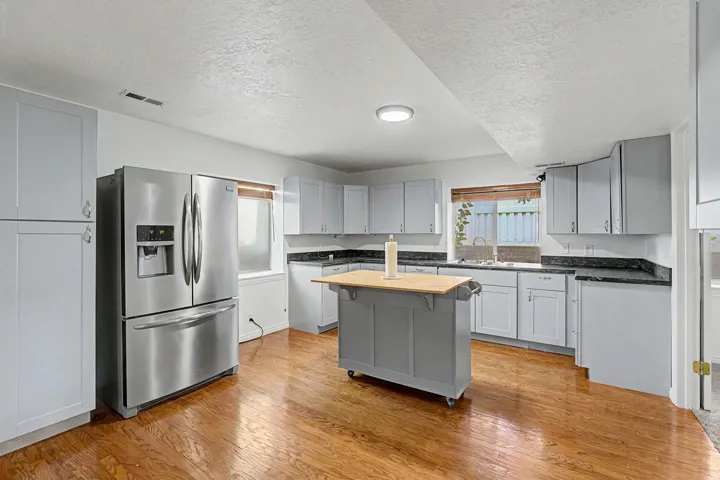 Spacious kitchen featuring white cabinetry, stainless steel French-door refrigerator with ice and water dispensers, black countertops, wood-finish flooring, and a center island with wooden countertop and storage