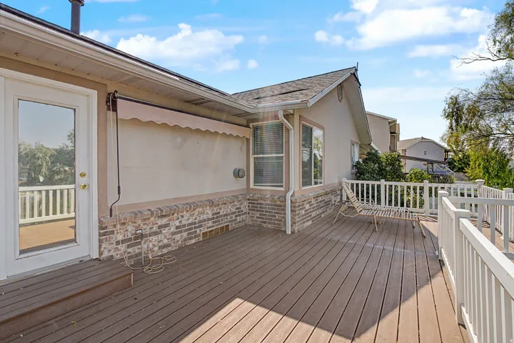 Expansive composite deck featuring composite decking with white vinyl railing, retractable awning for shade coverage, and direct access via glass sliding door from the home's interior