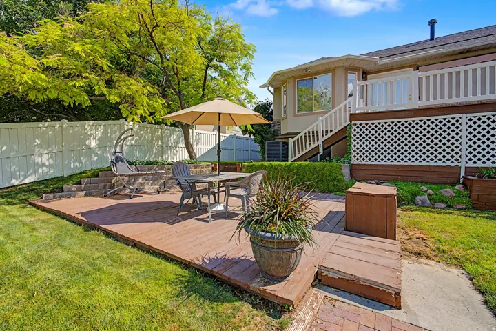 Expansive backyard featuring a wood-finish deck, white privacy fencing, mature trees, and a tiered landscaped area