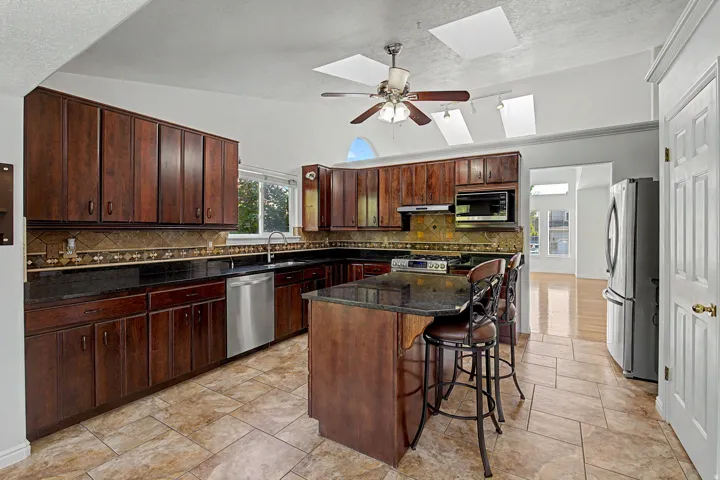 Kitchen featuring extensive dark wood-finish cabinetry, black countertops, stainless steel appliances, and a tiled backsplash