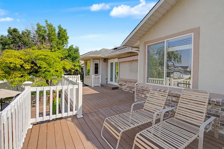 Expansive wood-finish deck with white railing, stucco exterior, and brick-finish foundation