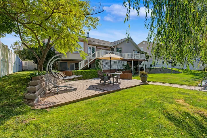 Expansive backyard featuring a manicured lawn, established trees, a multi-level deck with white railings, and a retaining wall
