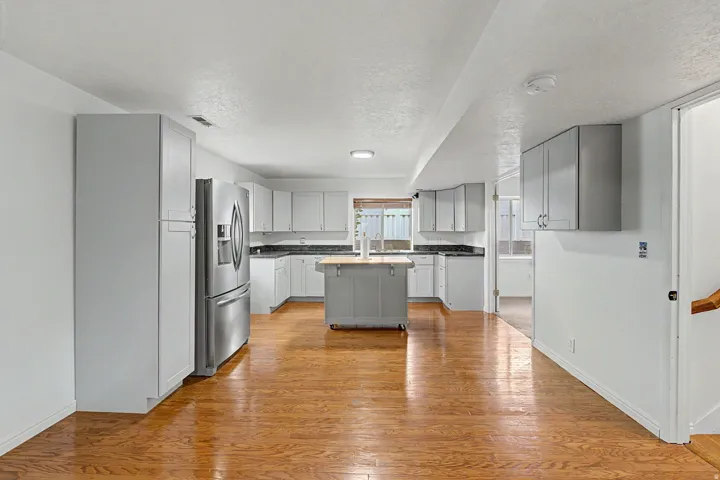 Spacious kitchen featuring white cabinetry, stainless steel French-door refrigerator, gas cooktop, and a central island with contrasting gray cabinetry