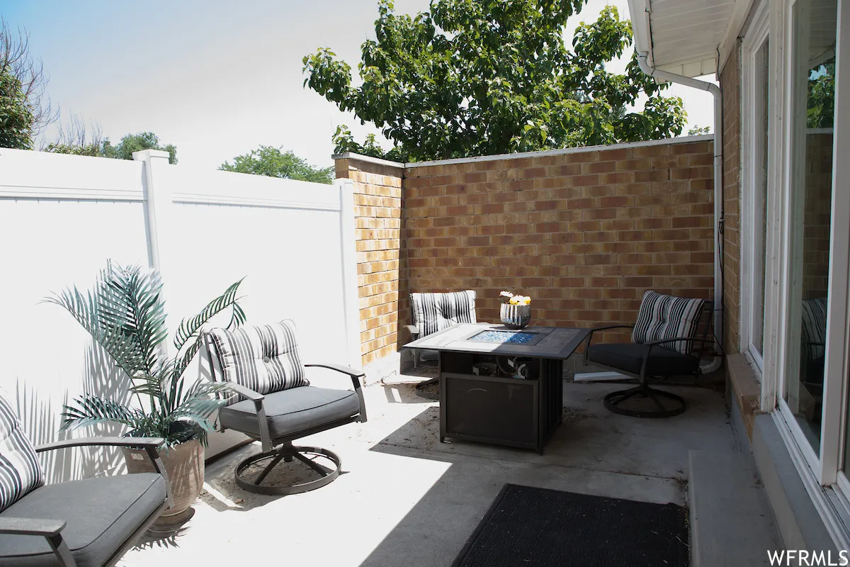 Private patio space featuring a concrete surface, white vinyl fencing, a brick privacy wall, and large windows
