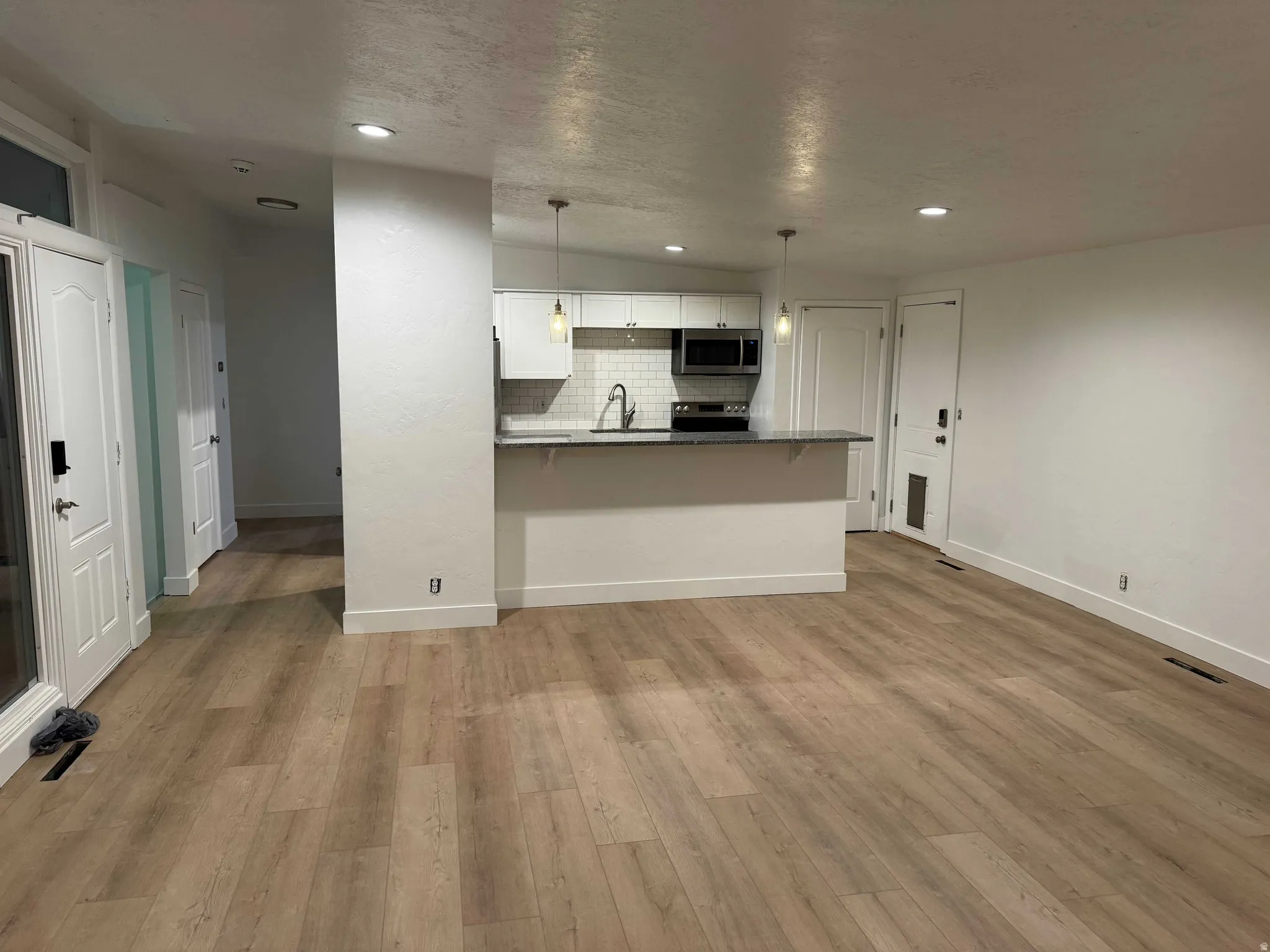 Wood-finish flooring throughout, kitchen with white cabinetry and dark countertops, stainless steel appliances, white subway tile backsplash, and recessed lighting