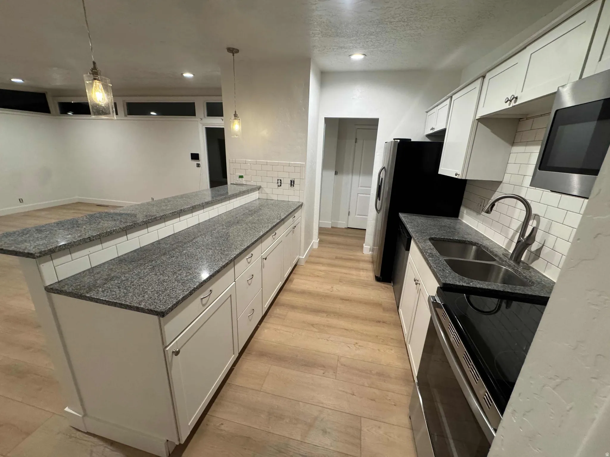 Kitchen featuring white cabinetry, granite countertops, subway tile backsplash, stainless steel sink with gooseneck faucet, and wood-finish flooring