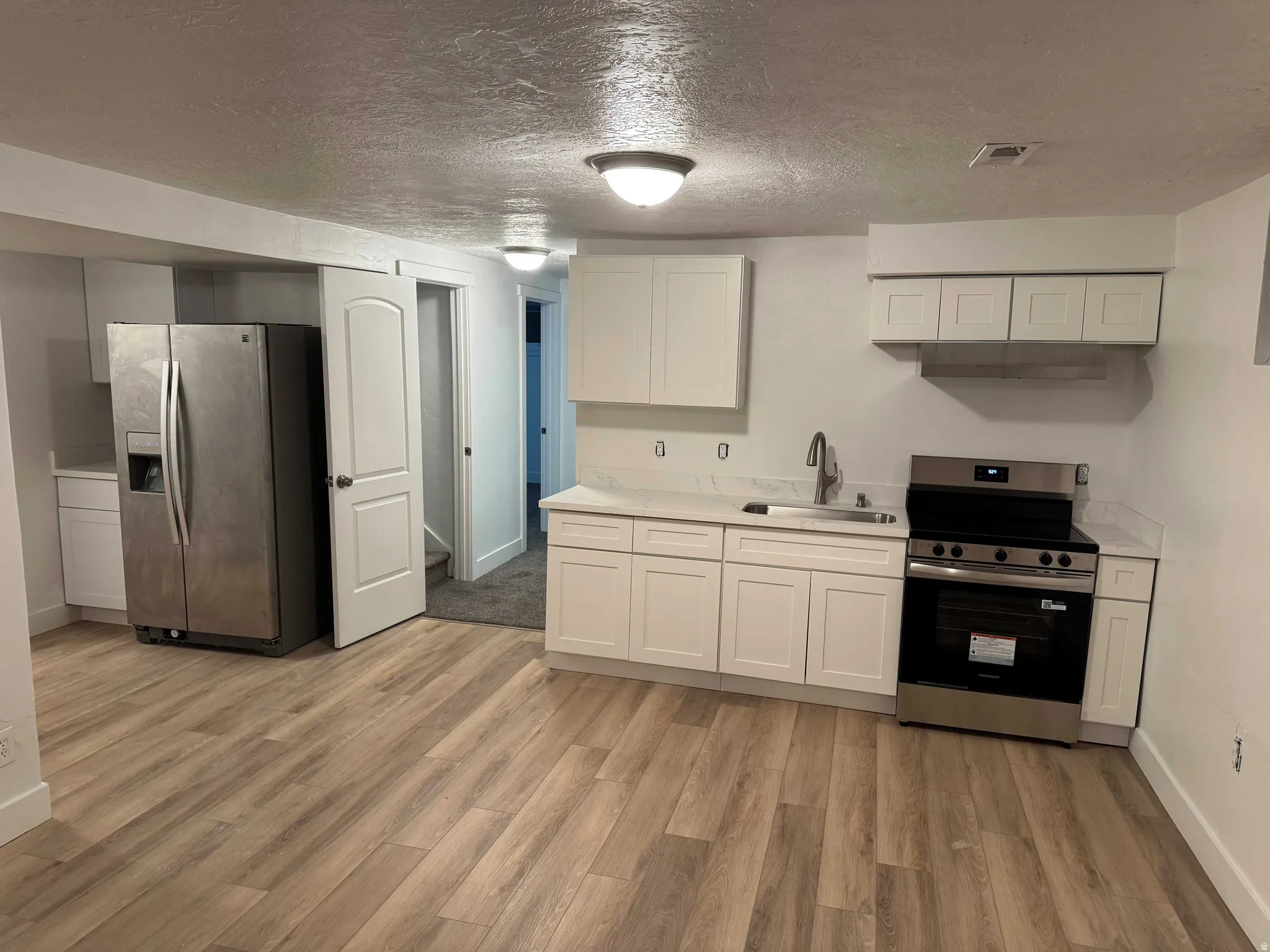 Full kitchen featuring white cabinetry, light-colored countertops, stainless steel appliances, and wood-finish flooring