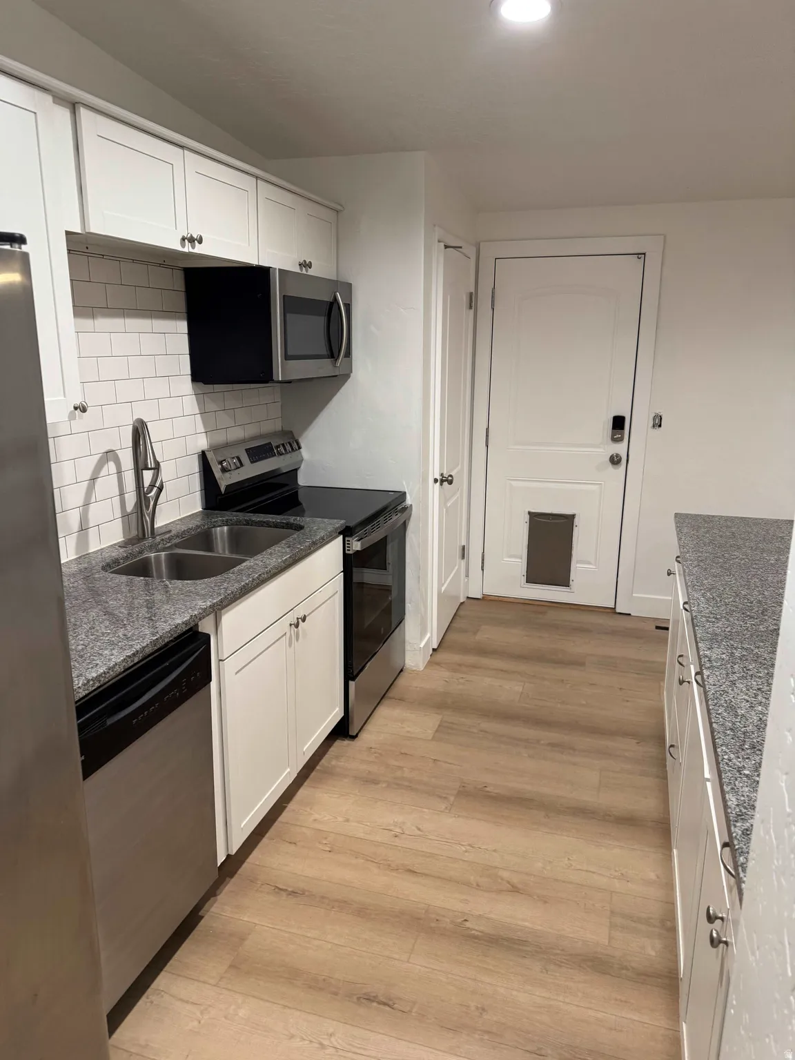 Kitchen featuring white cabinetry, stainless steel appliances, speckled countertops, and wood-finish flooring