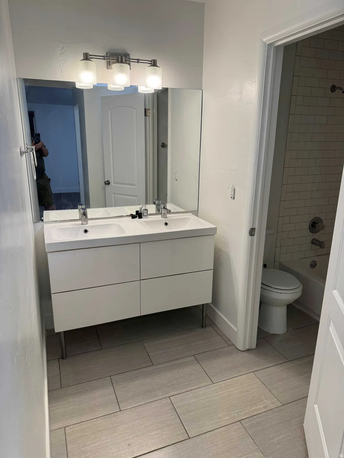 Dual vanity with integrated sinks, contemporary wall-mounted light fixture, large wall mirror, and rectangular tile flooring