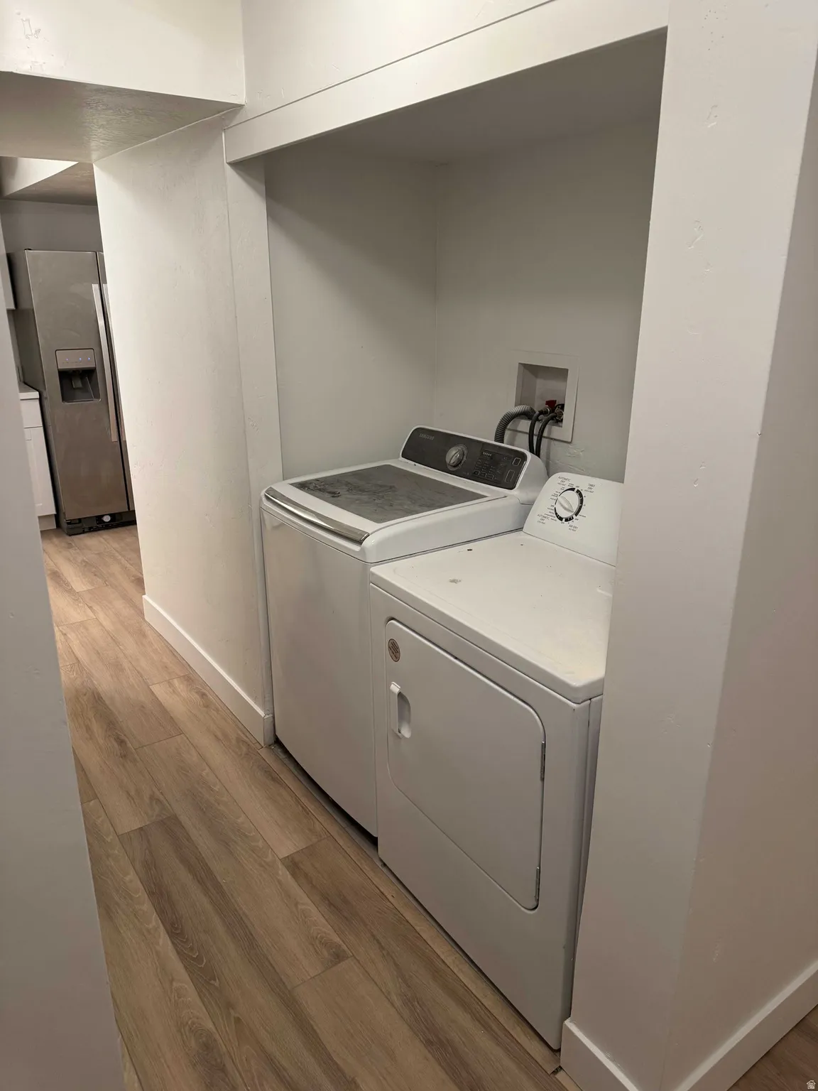 Dedicated laundry area with recessed shelving, wood-finish flooring, and crisp white walls