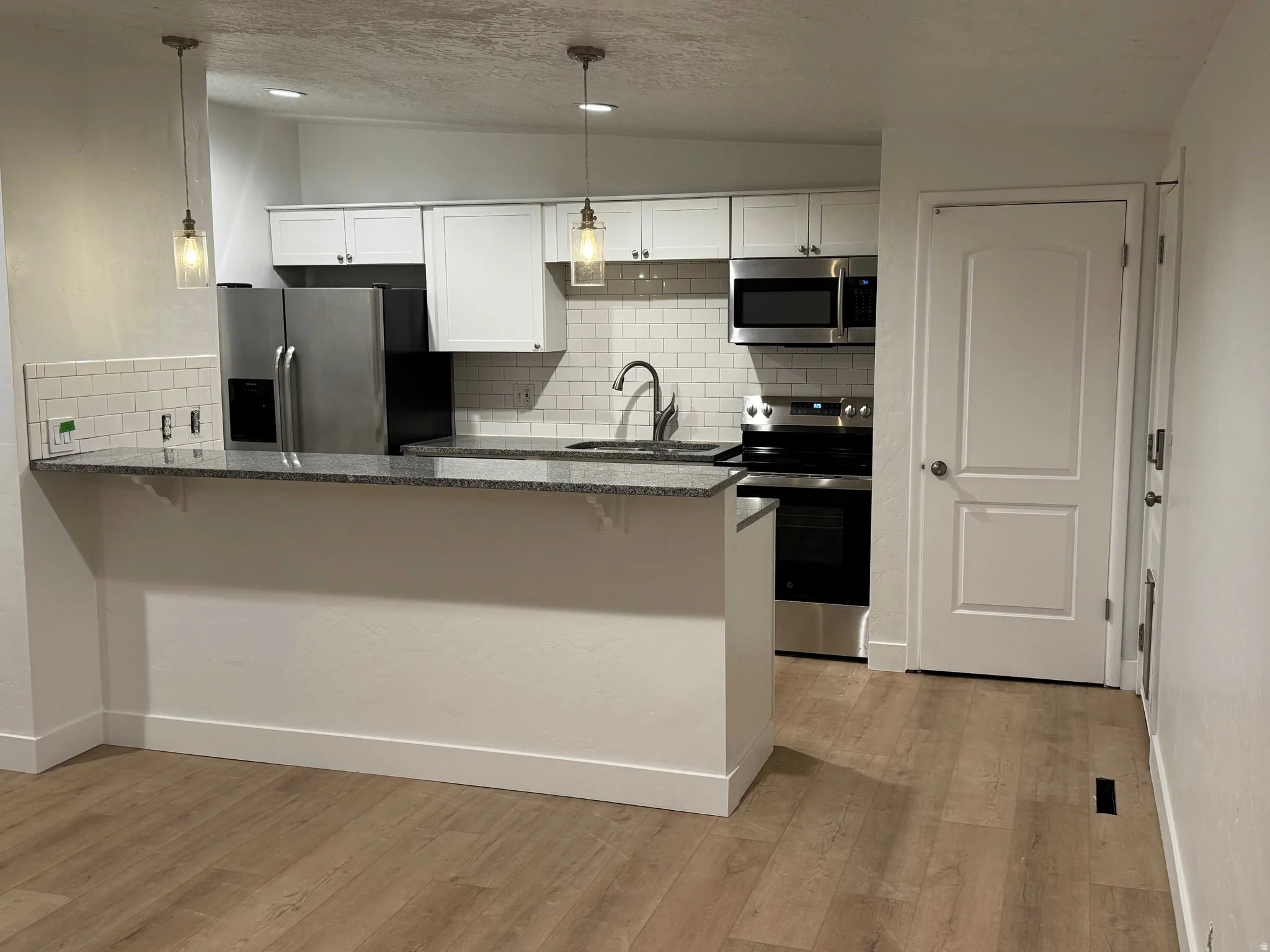 Kitchen featuring white cabinetry, subway tile backsplash, stainless steel appliances, and a breakfast bar with stone-finish countertops