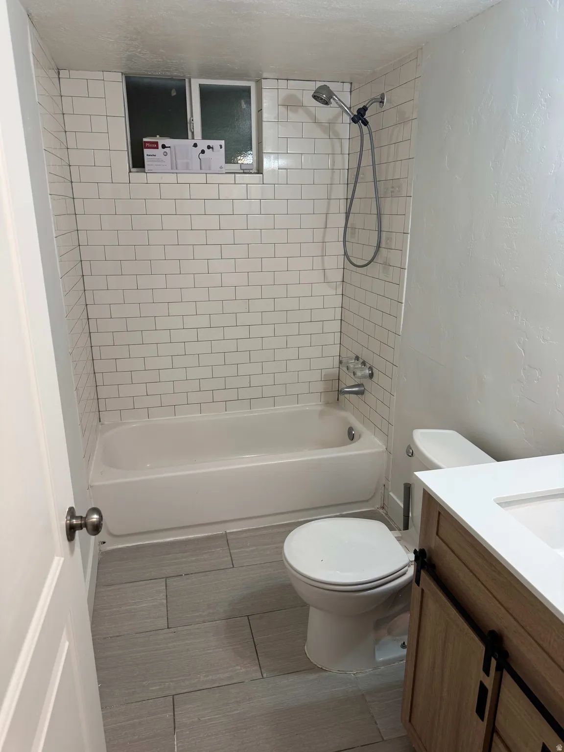 White subway tile shower surround with a built-in tub, chrome shower fixtures, and a window