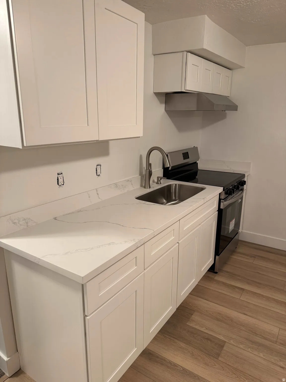 White shaker cabinetry with stone-finish countertops, stainless steel sink, contemporary faucet, and wood-finish flooring
