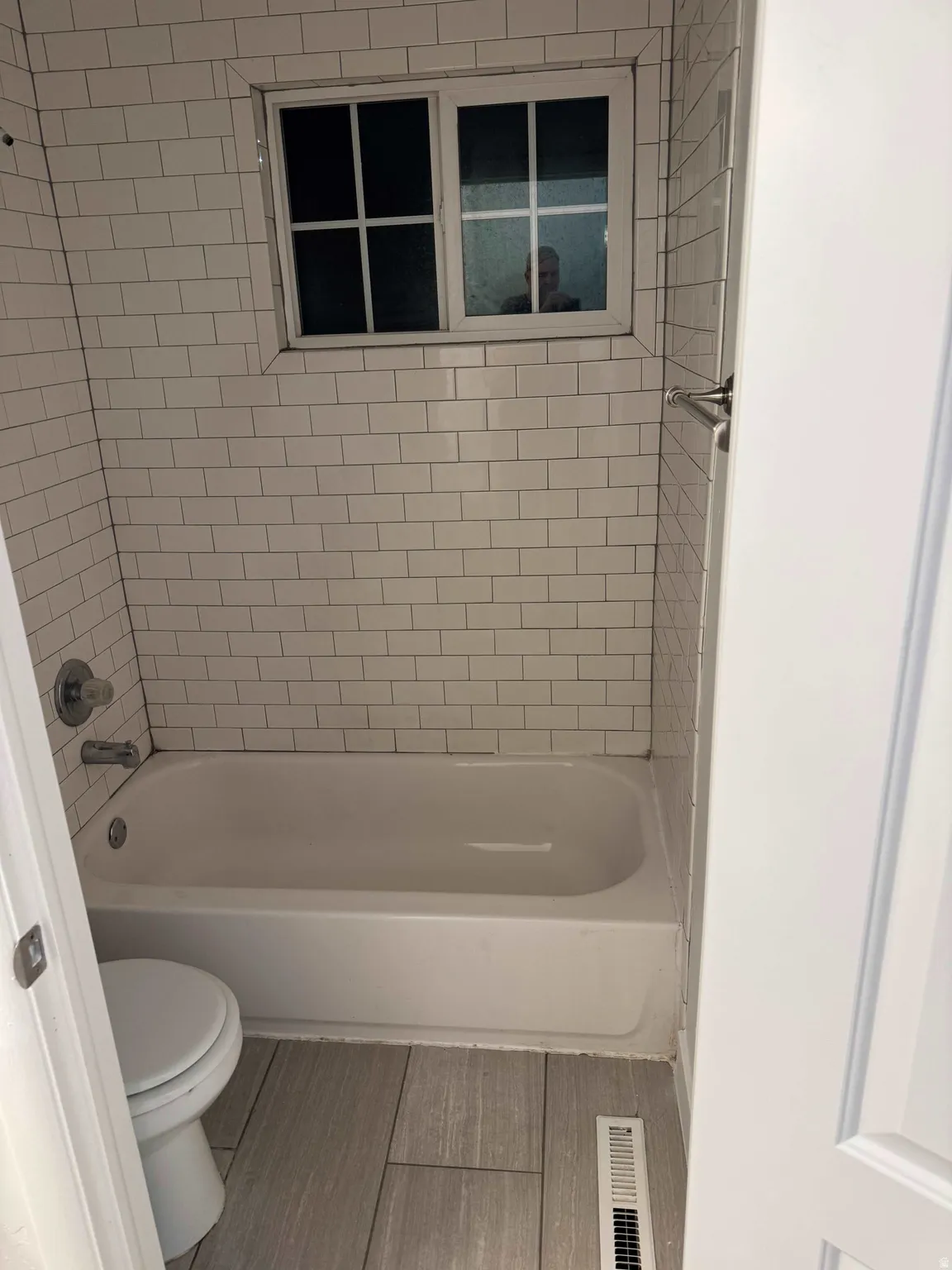 Bathroom featuring a white subway tile surround, white bathtub, chrome fixtures, and wood-finish floor tiling
