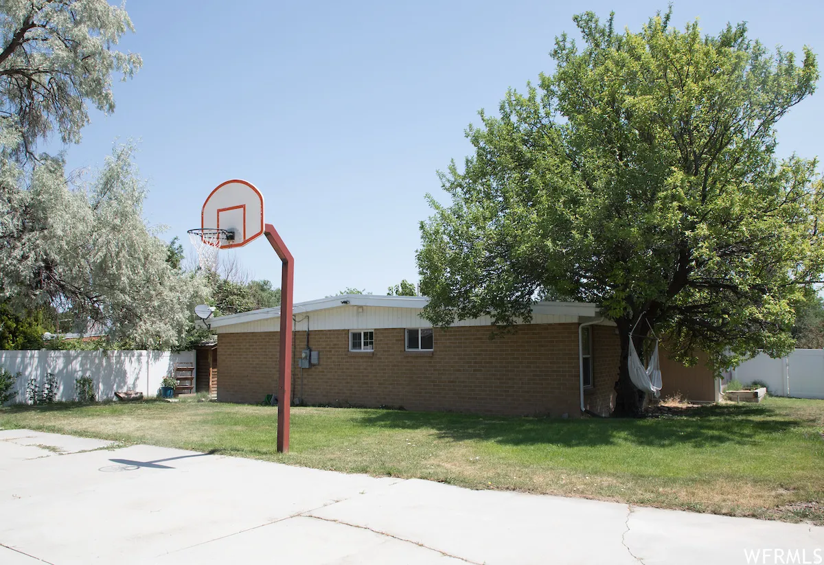 Expansive backyard featuring a concrete sports court with a basketball hoop, a manicured lawn, and mature trees