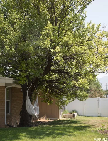 Expansive backyard featuring a mature tree, brick exterior, and white privacy fencing