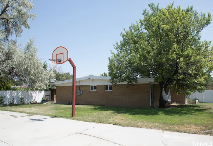 Brick exterior with white trim, large mature trees, and a concrete pad