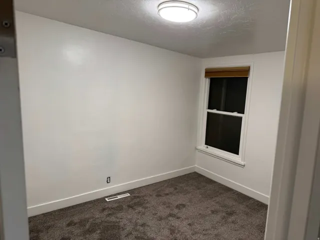 Recessed window with wood-finish blinds, wall-mounted light fixture, and carpeted flooring