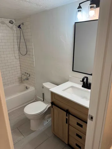 Bathroom featuring a subway tile shower surround, a white bathtub, a wood-finish vanity with a barn door style cabinet, a white countertop with an integrated sink, and matte black fixtures
