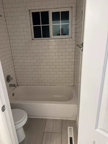 Bathroom featuring a white subway tile surround, white bathtub, chrome fixtures, and wood-finish floor tiling