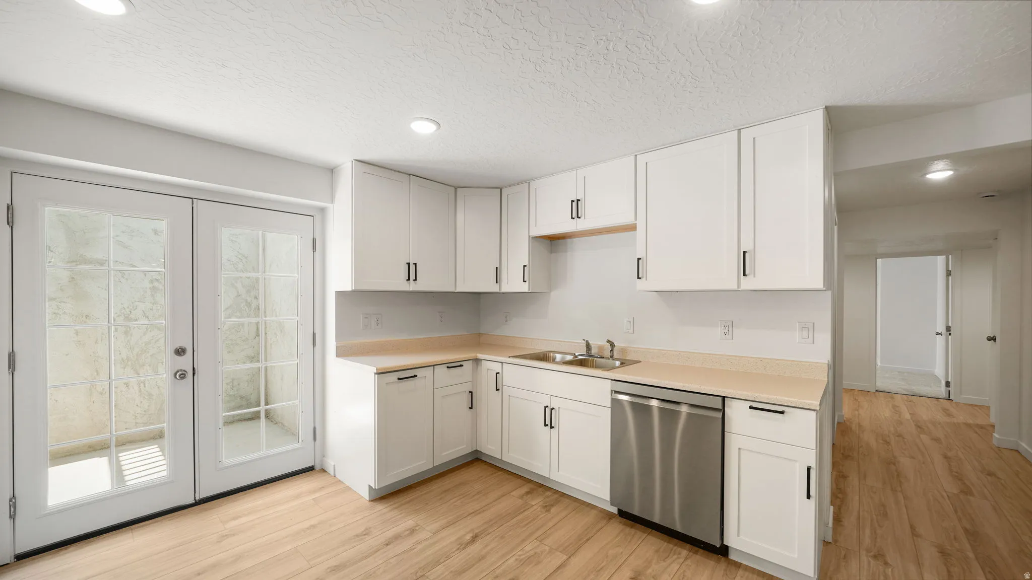 Kitchen featuring white cabinetry, light countertops, wood-finish flooring, stainless steel dishwasher, and French doors with divided lites