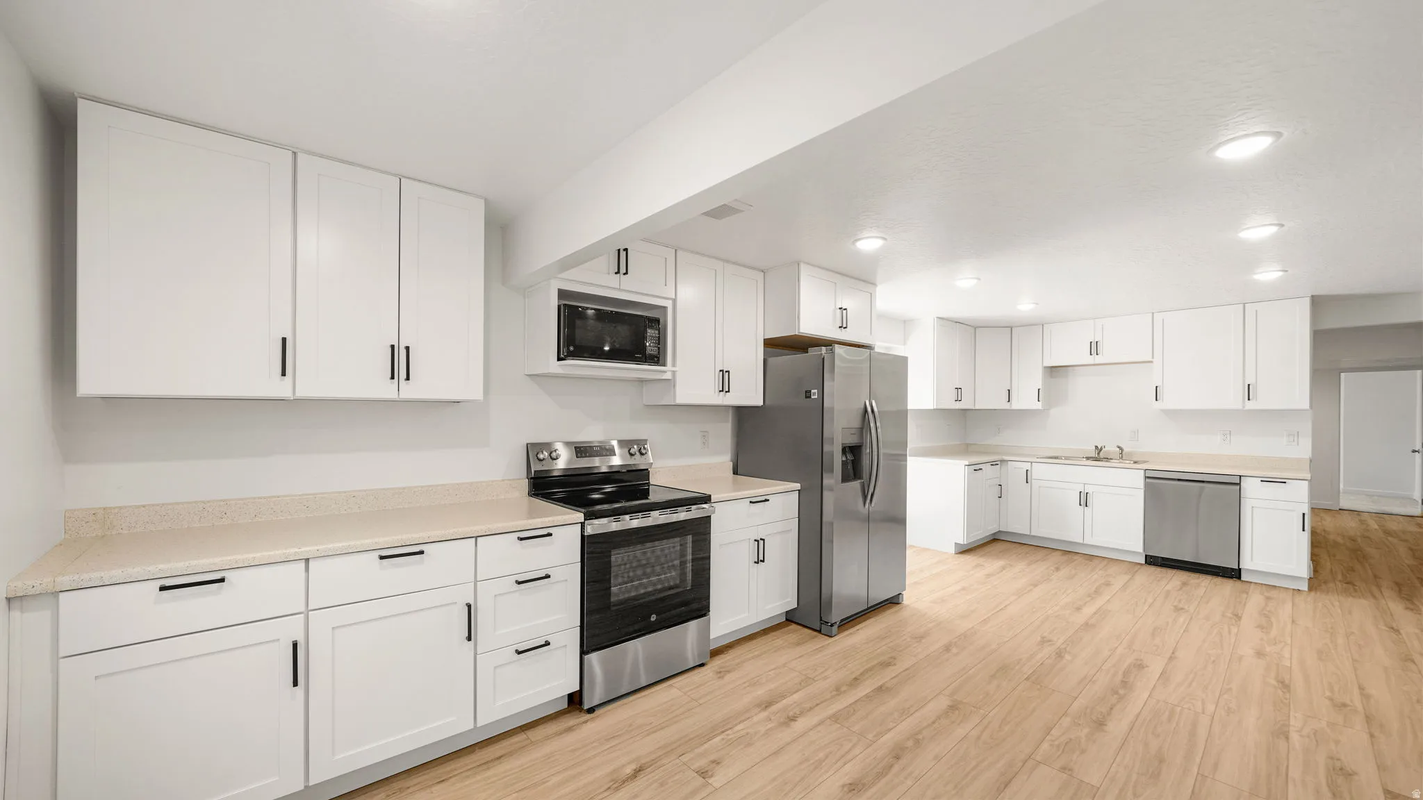 Kitchen featuring white cabinetry, light countertops, wood-finish flooring, stainless steel appliances, and recessed lighting.